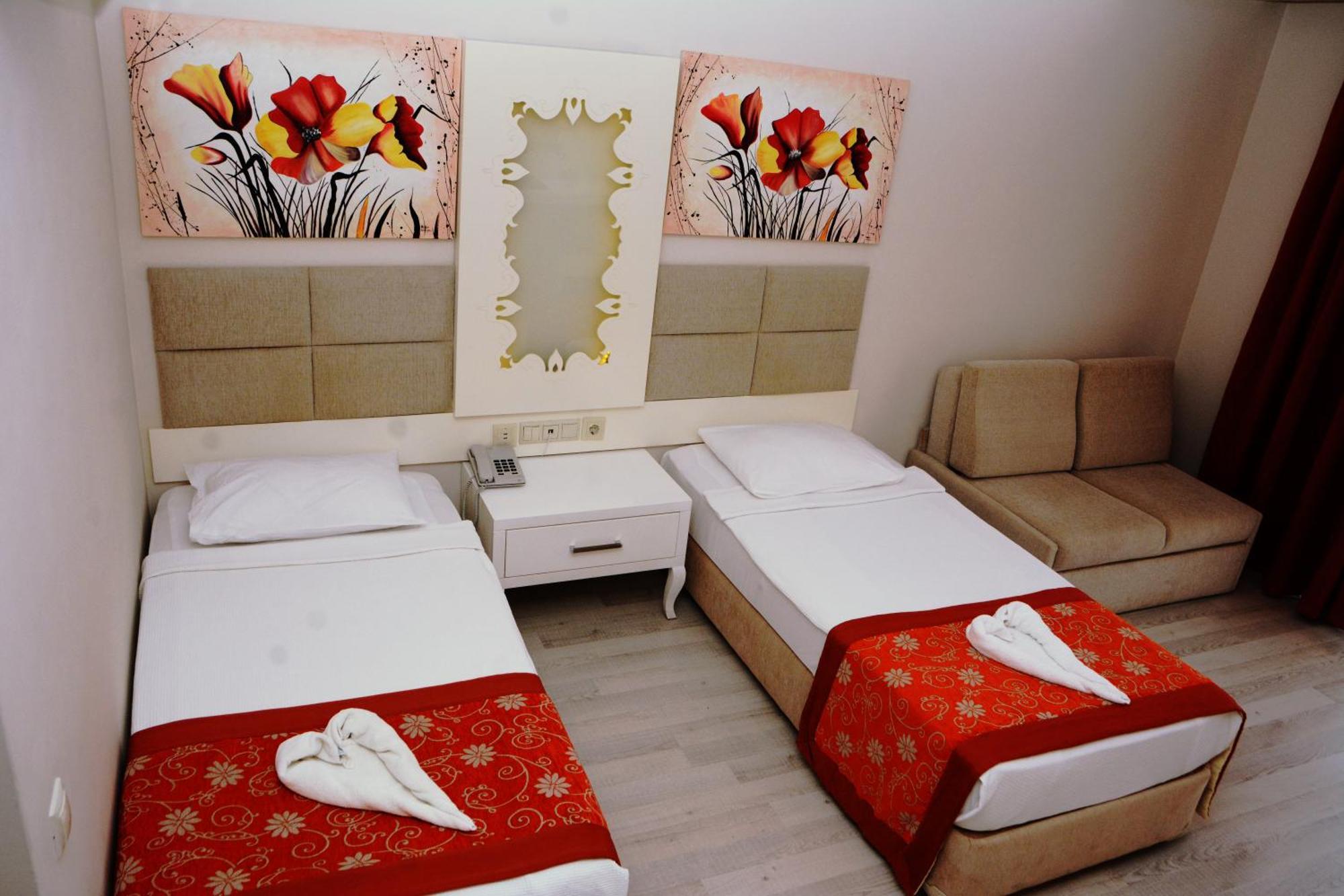 אנטליה Miramor Hotel & Spa מראה חיצוני תמונה The photo shows a hotel room featuring two single beds with white linens, each adorned with a decorative red throw. The headboards are upholstered in a light beige fabric. Above the beds, there are two large artwork pieces depicting colorful flowers.