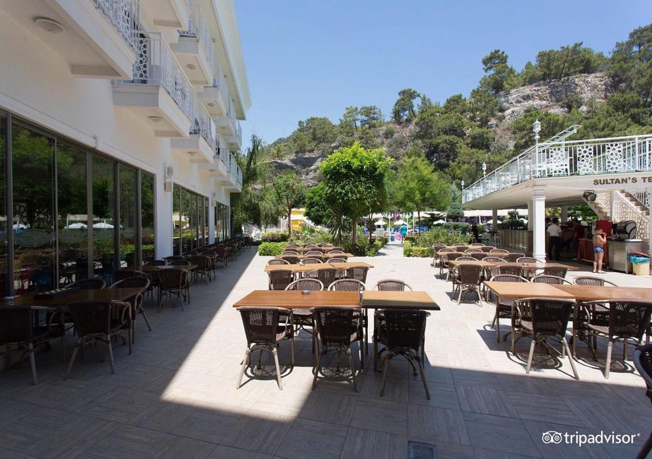 אנטליה Miramor Hotel & Spa מראה חיצוני תמונה The photo shows an outdoor dining area, likely at a restaurant or cafe. There are several tables with chairs arranged neatly on the paved ground, and some greenery, such as trees and plants, is visible in the background. The setting appears bright an